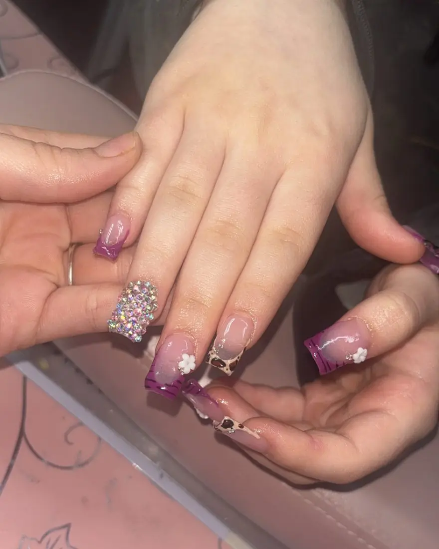 Purple french tips with a rhinestone accent nail, leopard print and small white flowers, done by Jade in Akron